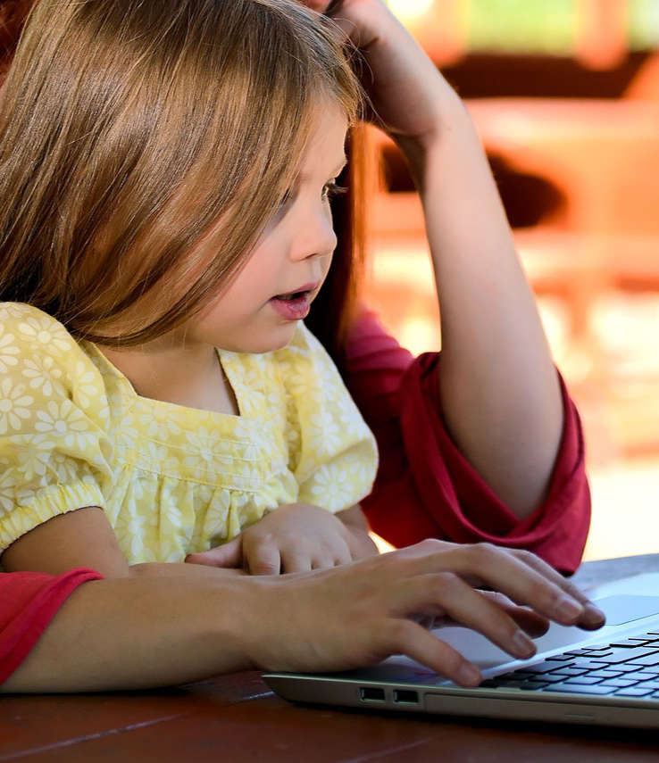 Mutter und Tochter sitzen gemeinsam an einem Laptop und schauen nach tollen Freizeitaktivitäten für Kinder auf Kidsdabei.